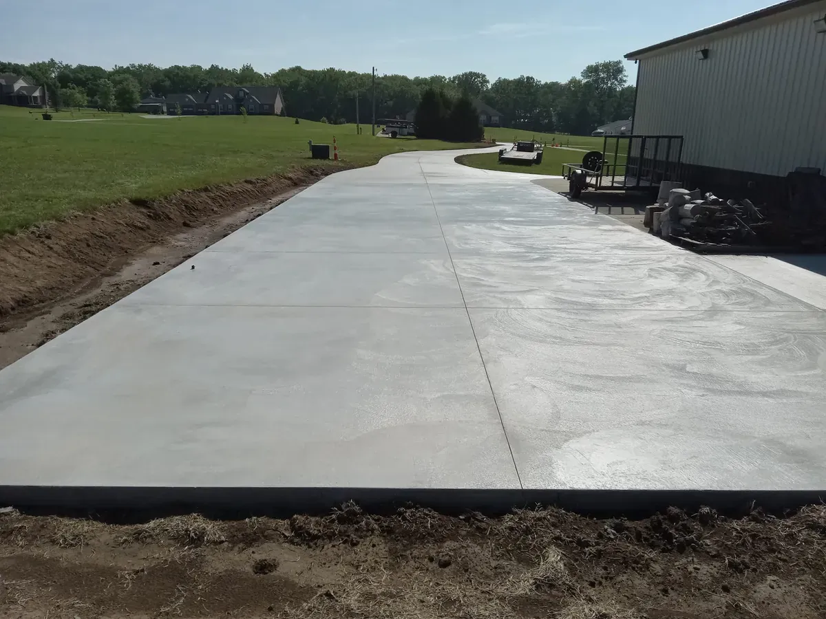 Long new broom-finish concrete slab poured beside a metal building on open land
